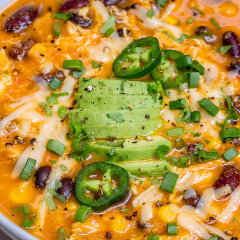 Close-up shot of Creamy Chicken Enchilada Soup with melted cheese, avocado slices, beans, and jalapeño.
