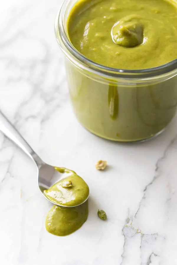 pistachio-butter-jar Close-up of pistachio butter in a glass jar with a spoonful on the side, showing its creamy texture.