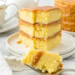 A close-up of a moist, three-layer caramel cake slice with caramel frosting between each layer, served on a white plate.