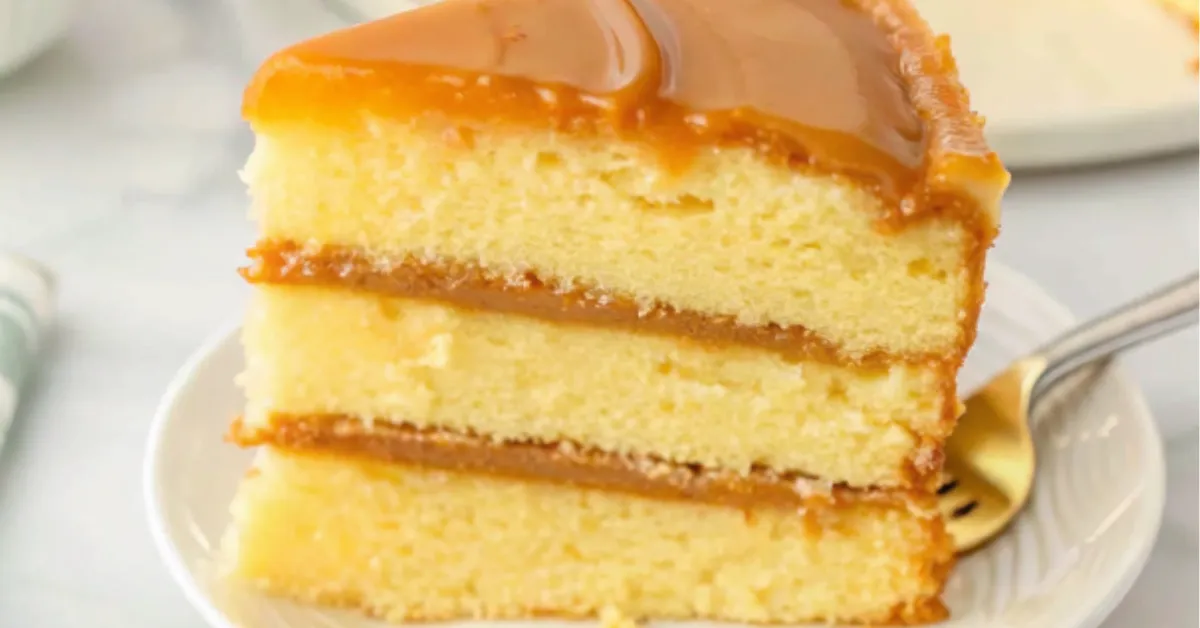 A slice of classic Southern caramel cake with rich caramel frosting between three moist vanilla cake layers on a white plate.