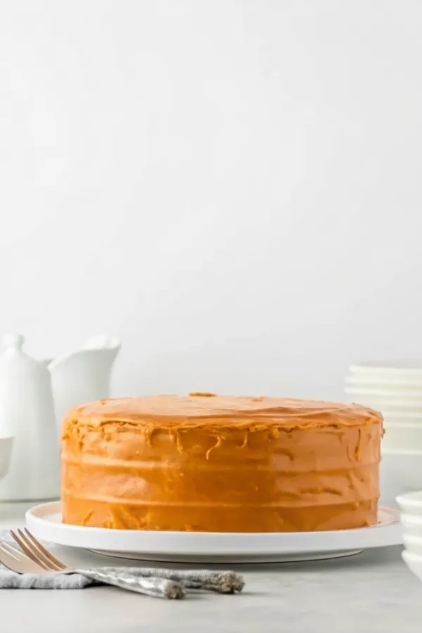 A whole homemade caramel cake covered in glossy caramel frosting, displayed on a white serving plate.